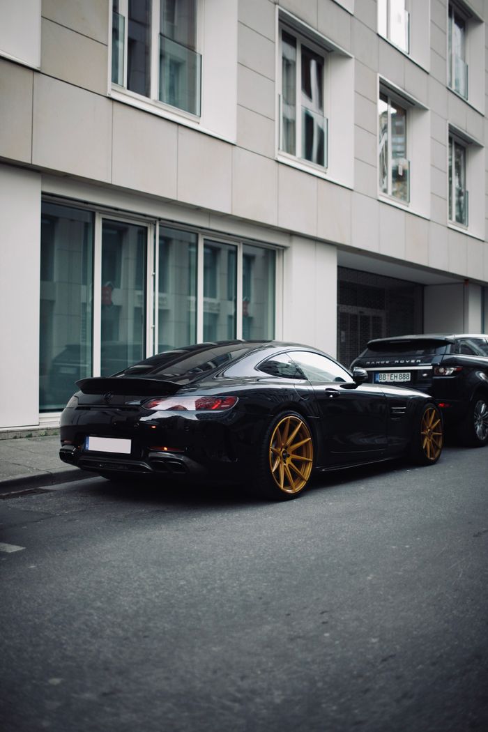 Home Black luxury car with golden rims parked on an urban street during the day.