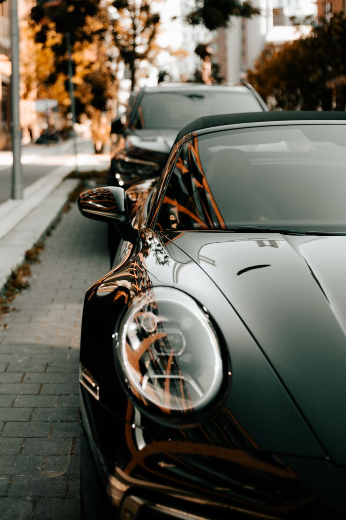 Offerings Sleek black sports car parked on a city street under autumn foliage, showcasing luxury design.